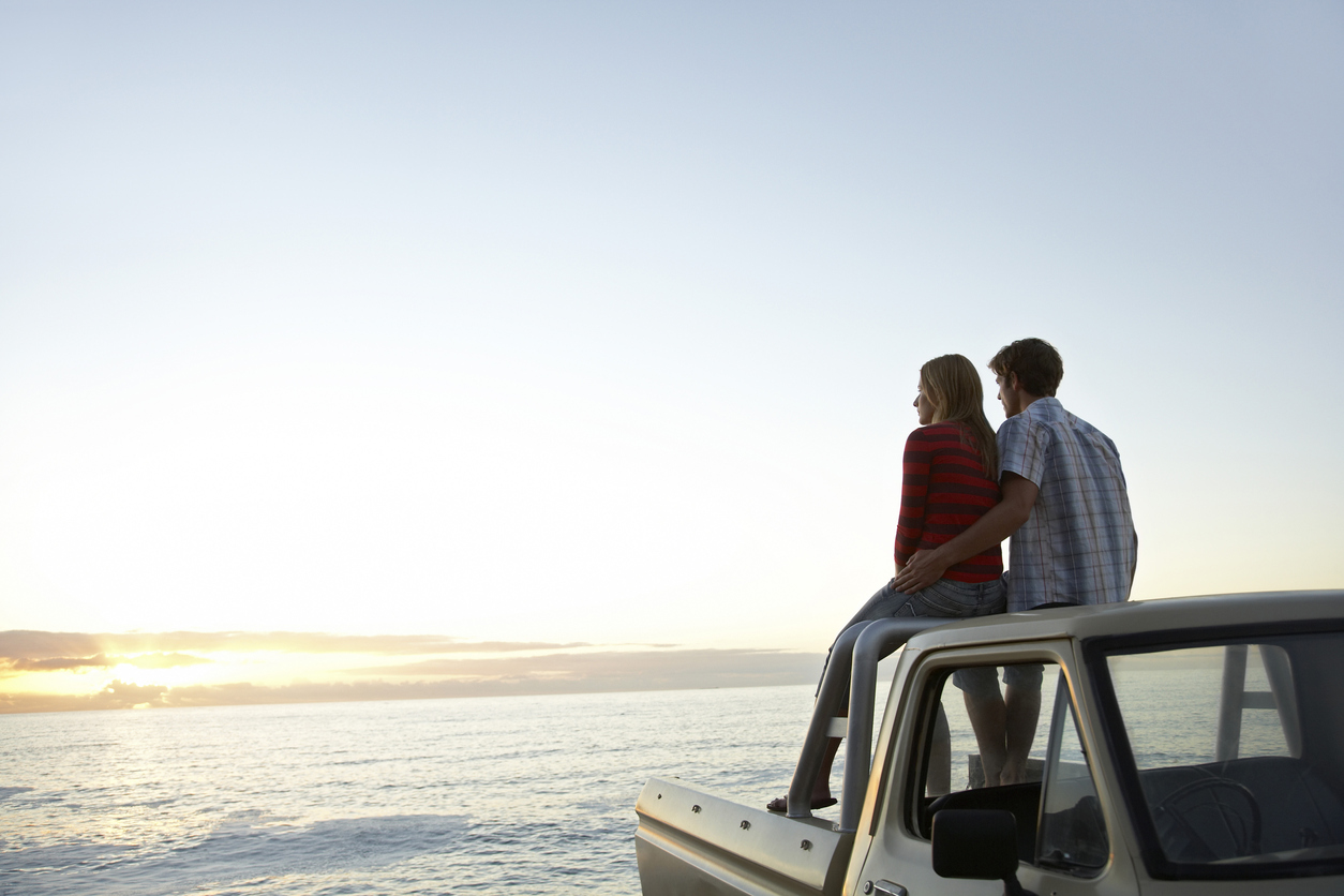 couple sitting on the back of a truck looking into the sunset