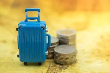 Blue miniature baggage with stack of coins on world map
