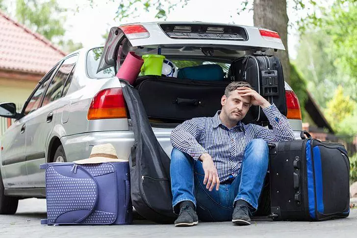 Stressed out man loading holiday suitcases into the car